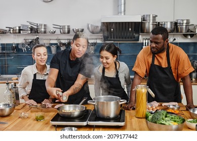 Portrait of female chef frying meat during cooking class with diverse group of people in kitchen interior - Powered by Shutterstock