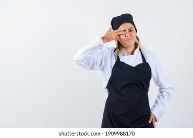 Portrait of female chef keeping fingers on eye in uniform, apron and looking amused front view 