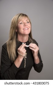 Portrait Of A Female Clergy Wearing A Black Shirt And Holding A Clerical Collar Which She Is Attaching To Her Shirt