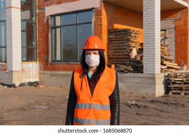 Portrait Of Female Construction Worker In Medical Mask And Overalls On Background Of House Under Construction.