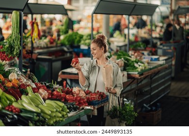 Portrait of female customer standing near market stall with paper shopping bag in her hands and buying fresh organic tomato at farmer's market. Shopper woman purchasing raw vegetable at green market. - Powered by Shutterstock