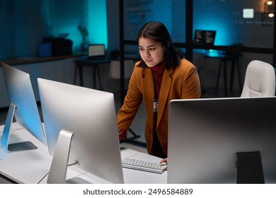 Portrait of female cybersecurity expert using computer with multiple monitors in office lit by blue light - Powered by Shutterstock - Get 15% off with code: PIKWIZARD15