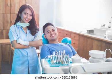 Portrait Of Female Dentist With Happy Male Patient At Clinic