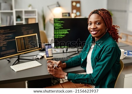 Portrait of female IT developer looking at camera and smiling against programming code on computer screen in office interior, copy space [[stock_photo]] © 