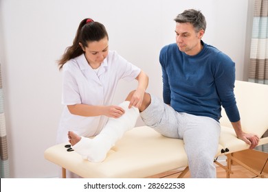 Portrait Of Female Doctor Bandaging Patient's Leg In Clinic