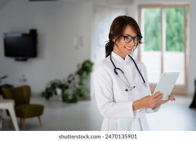 Portrait of a female doctor holding her patient chart on digital tablet while standing at the hospital corridor. - Powered by Shutterstock