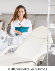 Portrait of female doctor in medical gown making notes in the patient medical history