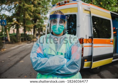 Portrait of a female doctor nurse in front of the ambulance with protective suit, gloves, mask and visor against the infection of Coronavirus, Covid-19 during her shift of service to the community