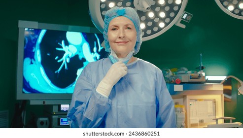 Portrait of female doctor in protective mask and hat in clinic. Nurse looking at camera and smiling in operating room. Adult woman tip the wink after successful operation in surgical department. - Powered by Shutterstock