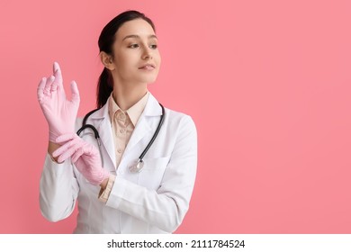 Portrait of female doctor putting on rubber gloves against pink background - Powered by Shutterstock
