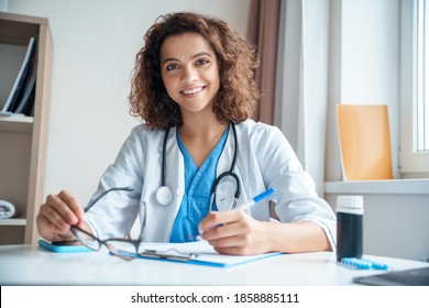 Portrait of female doctor sitting on work desk and smiling at camera. Telemedicine, Medical online, e health concept. Doctor using laptop for work, video call video chat with colleagues. Camera view. - Powered by Shutterstock