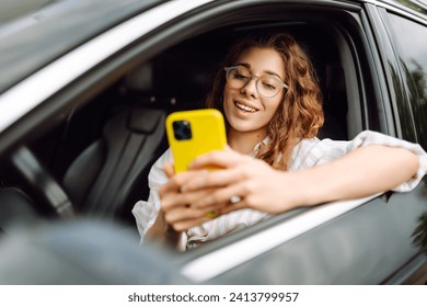 Portrait of a female driver uses a smartphone while driving a car. A young woman in a car uses a mobile phone to navigate. Movement concept, modern technology. - Powered by Shutterstock