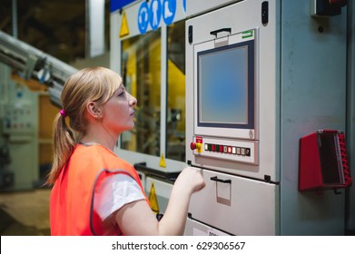 Portrait Of A Female Employee In An Orange Robe Vest In The Working Space Of A Production Facility, Supervises And Controls The Line In Food Production, Against The Background Of Equipment