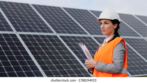 Portrait Of Female Engineer On Background Field Of Photovoltaic Solar Panels. Woman Technician At Solar Station.