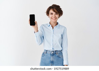 Portrait Of Female Entrepreneur Smiling And Showing Empty Smartphone Screen, Standing In Blue Collar Shirt On White Background.