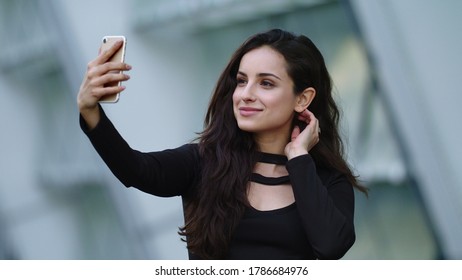 Portrait Female Entrepreneur Using Video Call At Street. Sexy Businesswoman Using Smartphone In Black Dress Outdoors. Attractive Woman Touching Hair With Phone In Hand Outside.