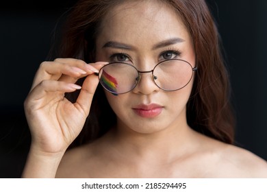 Portrait Of Female Face Wear Glasses With Colorful Painted Rainbow On Cheek And Looking At Camera. LGBT Flag. Equality And Support Of Diversities To People.