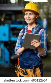 Portrait Of Female Factory Worker Wearing Hardhat Using Digital Tablet And Smiling, Looking Away