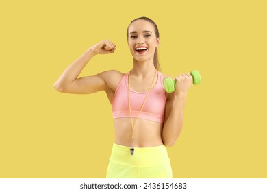 Retrato de entrenador de fitness femenino con mancuerna que muestra los músculos sobre fondo amarillo