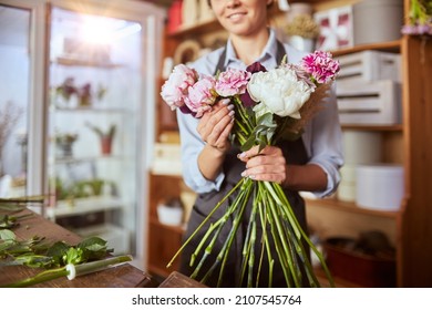 Portrait of female florist in apron arranging fresh flowers for bouquet in the flower shop, using roses, hydrangea, peonies. Small local business - Powered by Shutterstock