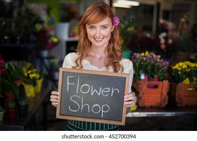 Portrait of female florist holding slate with flower shop sign in the flower shop - Powered by Shutterstock