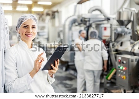 Portrait of female food factory inspector using tablet and smiling at the camera.