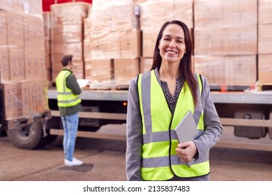 Portrait Of Female Freight Haulage Manager Standing By Truck Being Loaded By Fork Lift