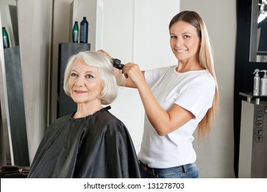 Portrait Of Female Hairdresser Ironing Senior Woman's Hair In Salon