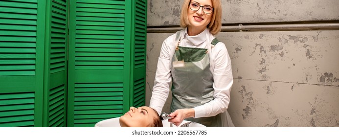 Portrait Of Female Hairdresser Washing Hair Of The Young Caucasian Woman In A Beauty Salon