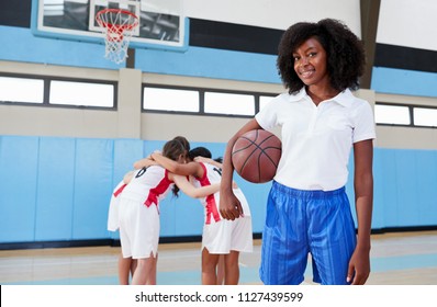 Portrait Of Female High School Basketball Coach With Team Huddle In Background