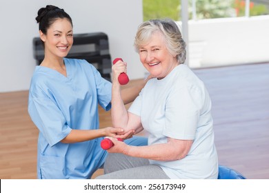 Portrait of female instructor assisting senior woman in lifting dumbbells at gym