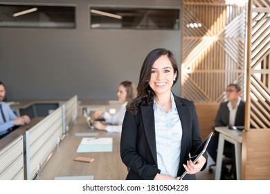 Portrait of female lawyer holding digital tablet standing in office with colleagues working in background