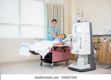 Portrait Of Female Nurse By Patient Receiving Renal Dialysis In Hospital Room