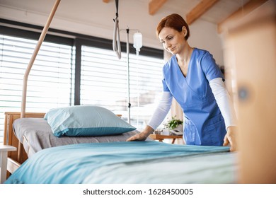 Portrait Of Female Nurse Or Housekeeping Staff Changing Sheets In Hospital.