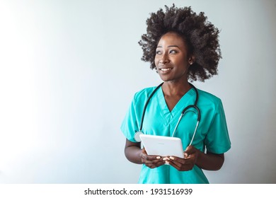 Portrait Of Female Nurse Using Tablet At Hospital. Female Nurse Or Doctor Smiles While Staring Out Window In Hospital Hallway And Holding Digital Tablet With Electronic Patient File