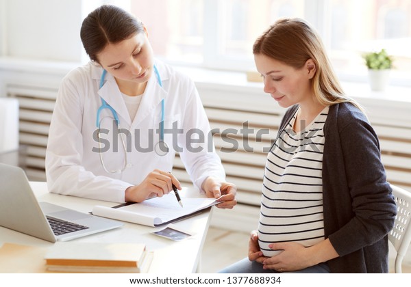 Portrait of female obstetrician consulting\
pregnant woman in doctors office, copy\
space