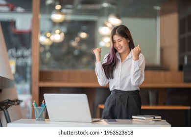 Portrait of female office worker celebrating her accomplishment while standing at the office table.	 - Shutterstock ID 1953523618