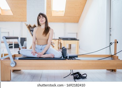 Portrait of female owner of small pilates studio wearing sportswear posing on sports equipment, reformer bed with light interior on background. - Powered by Shutterstock