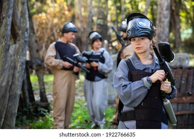 Portrait of female paintball sport player holding shooting gun and her team on background