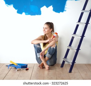 Portrait Of Female Painter Sitting On Floor Near Wall After Painting.