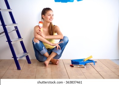 Portrait Of Female Painter Sitting On Floor Near Wall After Painting.