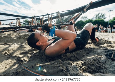 Portrait of a female participating in an obstacle course race outdoor while crawling under the ladder on a sand. Wearing trail running shoes with good grip and gloves for protection. - Powered by Shutterstock