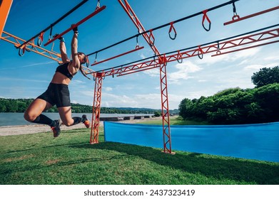 Portrait of a female participating in an obstacle course race outdoor while using suspensions. Wearing moisture-wicking clothing, trail running shoes with good grip and gloves for protection. - Powered by Shutterstock