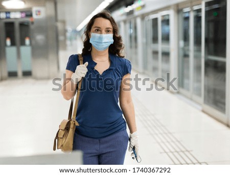 Portrait of female passenger in disposable face mask and latex gloves waiting for train on subway platform. Concept of prevention and social distancing in coronavirus pandemic
