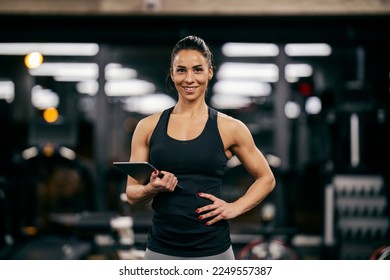 Portrait of a female personal trainer holding tablet and smiling at the camera in a gym. - Powered by Shutterstock