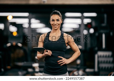 Portrait of a female personal trainer holding tablet and smiling at the camera in a gym.