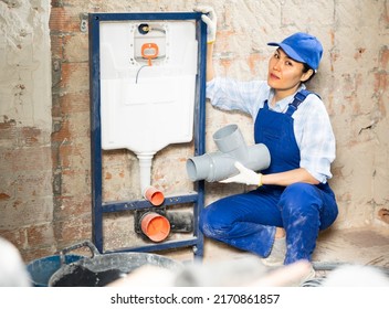 Portrait Of Female Plumber In Blue Overall Holding A Plastic Sewer Pipe, Next To A Sewerage System Being Installed