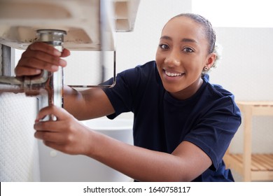 Portrait Of Female Plumber Working To Fix Leaking Sink In Home Bathroom