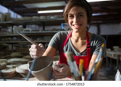 Portrait of female potter carving mug in pottery workshop - Powered by Shutterstock