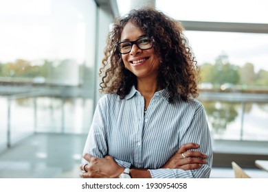 Portrait of female professional with curly hair wearing eyeglasses. . Smiling businesswoman with her arms crossed